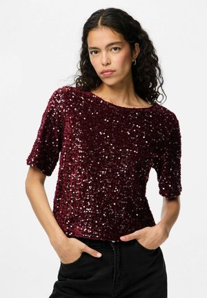 Top burdeos con lentejuelas, de mangas cortas y escote redondo, que presenta una superficie texturizada y una silueta ajustada. Combinado con pantalones negros.
