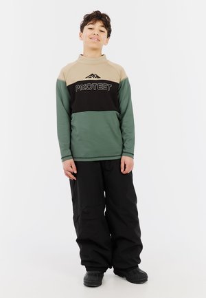 Lange mouw shirt in beige, zwart en groen met een bergafbeelding en "PROTEST" logo. Draagt een losse zwarte broek en stevige zwarte schoenen.