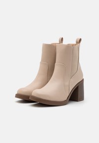 Beige kotníkové boty s hladkým koženým povrchem, elastickými postranními panely a masivním hnědým podpatkem. Plná gumová podrážka pro lepší přilnavost.