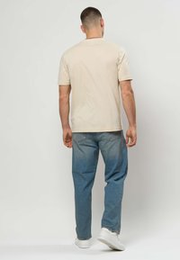 Béžové tričko s krátkym rukávom a rovný strih, doplnené svetlomodrými džínsami a bielymi teniskami. Jednofarebná látka bez viditeľných vzorov.