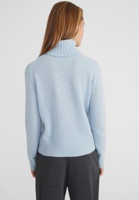 Hellblauer Strickpullover mit Stehkragen, gerippten Bündchen und Saum sowie weicher Textur, kombiniert mit dunkelgrauen Hosen.