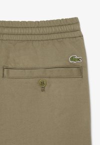 Spodnie khaki z elastycznym pasem, z tylną kieszenią zapinaną na guzik i zielonym haftowanym logo krokodyla nad kieszenią.