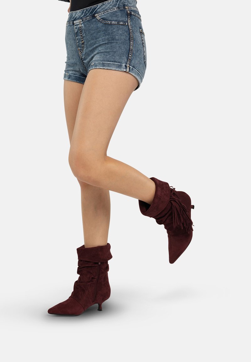 Donkerrode suède enkellaarsjes met een nonchalant ontwerp, een spitse neus en franjes aan de zijkant, gecombineerd met denim shorts.