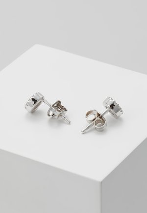 Petites boucles d'oreilles clous en argent avec un motif arrondi en forme de couronne sur une surface blanche inclinée.