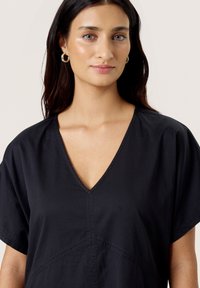 Black V-neck top with short sleeves, featuring a relaxed fit and seam detailing. Smooth fabric with minimal texture. No patterns or hardware.