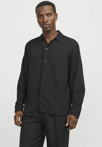 Zwarte langslavenshirt met een subtiel textuurpatroon, kraag en knoopsluiting aan de voorkant. De stof lijkt lichtgewicht en soepel.