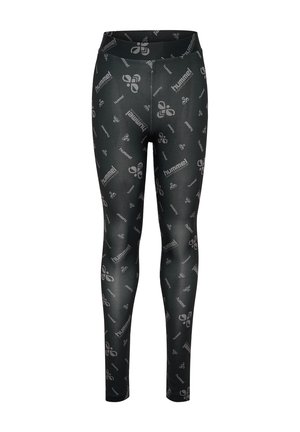 Jong meisje staat, draagt een roze oversized "hummel performance" t-shirt, zwarte patterned leggings, witte sokken en witte sneakers.