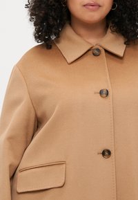 Καμηλό παλτό από μείγμα μάλλινου υφάσματος με κολάρο, δύο κουμπιά, πλαϊνές τσέπες και λεία υφή. Διαθέτει άνετη εφαρμογή και κλασικό σχέδιο.