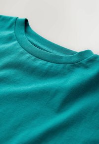 Türkisfarbenes Baumwoll-T-Shirt mit rundem Ausschnitt, glatter Textur und dezentem Stretch, das ein einfaches und sauberes Design zeigt.