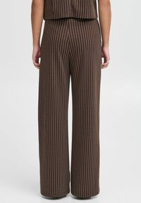 Pantalons large couleur marron avec des rayures verticales blanches, présentant une texture de tissu lisse et une taille haute. Aucun matériel ou accent proéminent.