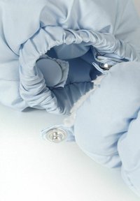 Svijetloplavi materijal s naboranom teksturom, zatvoren srebrnim dugmadi na preklop, otkrivajući mekani unutarnji podstavu.