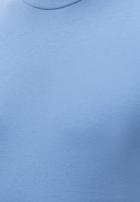 Φωτεινά γαλάζιο ύφασμα με λεπτή πλεκτή υφή και στρογγυλή λαιμόκοψη, δείχνει μια κοντινή λεπτομέρεια ενός ρούχου.
