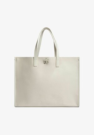 Grand sac fourre-tout beige clair en matériau texturé avec deux anses plates et un accent circulaire distinctif à l'avant.