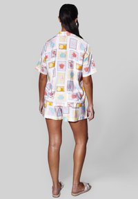 Mujer con cabello oscuro recogido en una coleta, vistiendo un conjunto de camiseta de manga corta y pantalones cortos en tonos pastel con estampados de conchas marinas y corales.
