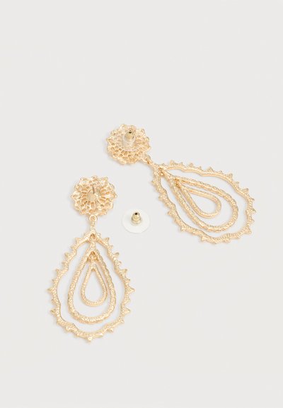 Arany tónusú filigrán fülbevalók, három egymásba ágyazott csepp alakú formával és biztonságos, tolószáras zárral, egyszínű háttéren.