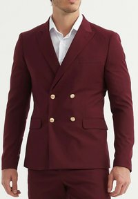 Veste de costume bordeaux à double boutonnage avec des boutons dorés, des revers crantés et une poche poitrine unique. Confectionnée en tissu lisse.