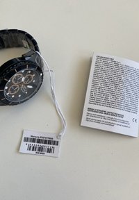 Orologio cronografo nero con finitura lucida, tre sottoquarti e dettagli in oro rosa. Include etichetta di garanzia e manuale di istruzioni nelle vicinanze.