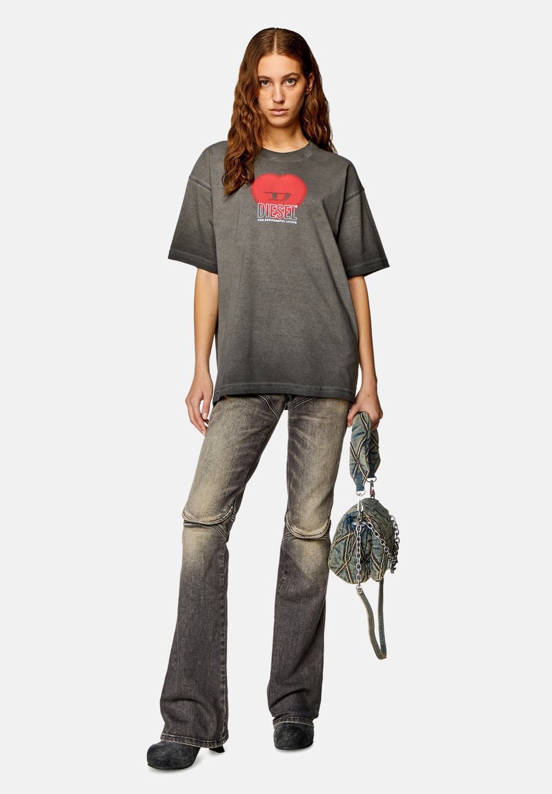 Tricou oversized gri cu grafică roșie cu buze și logo. Blugi gri estompați, evazați, cu detalii la cusătura genunchiului. Poartă o geantă mică texturată.