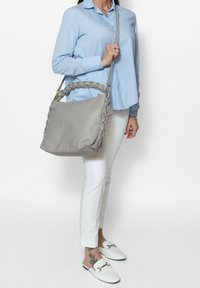 Borsa tote grigia con manico intrecciato, una texture liscia e un design spazioso. La borsa è portata a spalla.