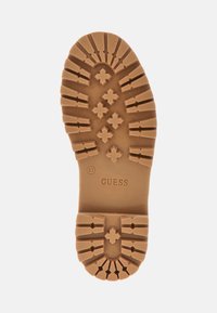 Suola in gomma con una superficie strutturata e robusta. Presenta un motivo di croci e linee, etichettato "Guess" e taglia "37" sul tallone.