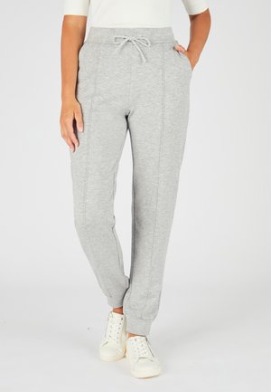 Grijze trainingsbroek met een tailleband met trekkoord, taps toelopende pijpen, zijzakken en zichtbare stikseldetails, gecombineerd met witte sneakers.