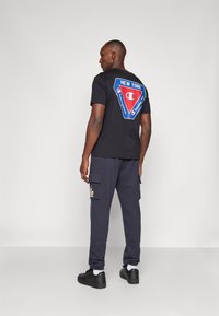 Svart bomullströja med en färgglad triangelgrafik och texten "NEW YORK" på baksidan. Kombinerad med marinblå cargo-byxor och svarta sneakers.