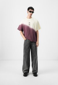 Lätt t-shirt med kort ärm i krämfärgad och burgundy färgblock, med grafisk design; tillsammans med lösa svarta jeans. Strukturerad, avslappnad look.