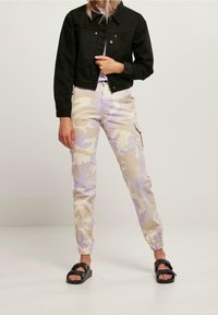 Svart cropped denimjacka över ljuslila och beige camouflagedelar byxor med elastiska manschetter. Svarta sandaler med remdetails.