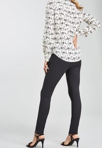 La blouse présente un fond blanc avec un motif abstrait noir, des manches longues et un col. Le pantalon est noir, moulant et avec des fentes à la cheville.