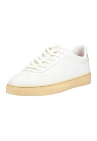 Bílá nízká teniska s béžovou gumovou podrážkou a bílými tkaničkami, hladký kožený svršek, nakloněná tak, aby ukázala vnější stranu a předek.