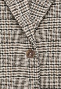 Tweed sako s houndstooth vzorem v béžové, hnědé a černé barvě se zdobným hnědým knoflíkem vpředu.