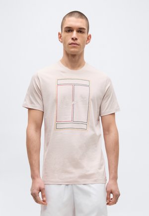 Joven con una camiseta beige claro con un diseño rectangular multicolor cosido y un logo central de Nike swoosh, combinado con pantalones cortos blancos.