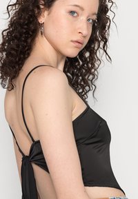 Top cropped de cetim preto com alças finas, costas descobertas e um detalhe atado na cintura, exibindo uma textura suave e um design ajustado.
