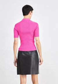 Figurbetontes, geripptes pinkes Strickpolo mit kurzen Ärmeln, kombiniert mit einem schwarzen Leder-A-Linien-Rock. Glatte Textur, schlichtes Design, keine sichtbaren Beschläge.