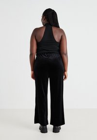 Top negro con tirantes y espalda al aire, combinado con pantalones anchos de terciopelo negro. La modelo lleva botas de plataforma negras y gruesas.
