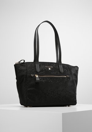 Czarna torba typu tote marki Michael Kors z kwiatowym wzorem, dwoma paskami na ramię, przednią kieszenią na zamek oraz detalami w kolorze złotym, takimi jak logo i zamek.