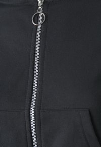 Czarna hoodie z zamkiem błyskawicznym, z metalowym srebrnym zamkiem i przednią kieszenią. Tkanina wydaje się miękka o gładkiej fakturze.