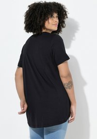 Czarny T-shirt z krótkim rękawem wykonany z miękkiej tkaniny, o luźnym kroju i przedłużonym dole, zestawiony z jasnoniebieskimi obcisłymi jeansami.