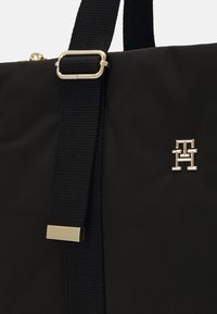 Sort nylon taske med tekstureret rem. Har en spænde og detaljer i guldfarvet metal med et fremtrædende logo. Enkel og funktionel.