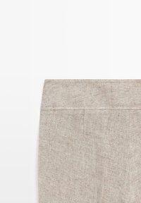 Beige linen pants showcasing the waistband and back seam, highlighting the fabric texture and stitching details on a white background.