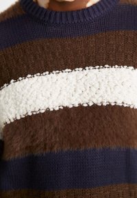 Brun, marinblå och krämfärgad randig tröja med en texturerad krämfärgad remsa i en fluffig stickning. Ribbad halsringning och detaljerad mjuk textur.