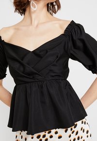 Černá off-shoulder blůza s vyšívanými rukávy, s přiléhavým korzetem a nabíraným peplum lemem. Hladká tkanina s mírným leskem.