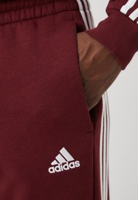 adidas Sportswear ESSENTIALS TAPERED CUFF 3-STRIPES  - Treniņtērpa apakšdaļas - shadow red