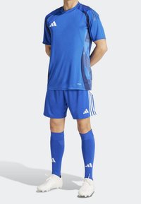 Blå idrottströja och shorts med geometriskt mönster, vita detaljer och logotyp. Inkluderar matchande blå strumpor och vita fotbollsskor.