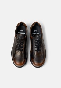 Brown leather shoes with a smooth finish, featuring black laces, rounded toe, and a contrasting black rubber sole. "Camper Pelotas" branding inside.