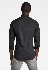 Camicia nera a maniche lunghe con bottoni, realizzata in tessuto morbido, con colletto classico, maniche arrotolate e orlo curvo.