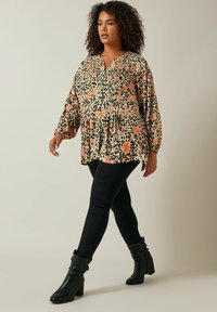Blomstermønstret og dyremønstret bluse i beige og sort med plisséer, parret med sorte skinny jeans og sorte hælisede ankelstøvler.