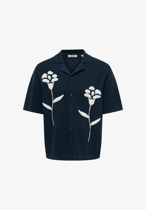 Camicia blu navy a maniche corte con bottoni e colletto, con due grandi motivi floreali bianchi sul davanti.