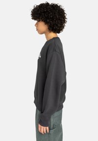 Zwart sweatshirt met ribgebreide manchetten en halslijn, met een zijprofielweergave. Draagt met groene cargobroeken, die een gestructureerde stof onthullen.