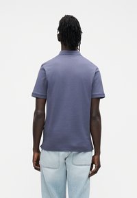 Polo azul-marinho com textura suave, mangas curtas e gola clássica, combinado com jeans azul-claro com bolsos traseiros.